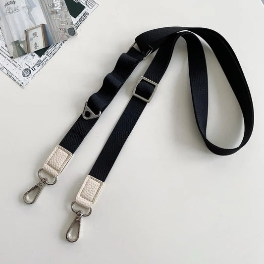Black crossbody strap with silver hardware on a white surface