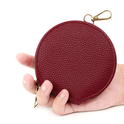 Round red leather coin purse with gold zipper held in a hand against a white background