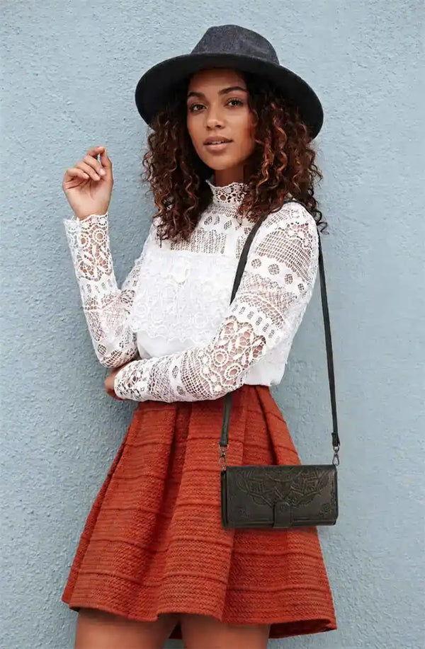 Woman wearing a lace top and red skirt with a black hat in black crossbody wallet phone case against a light blue wall.