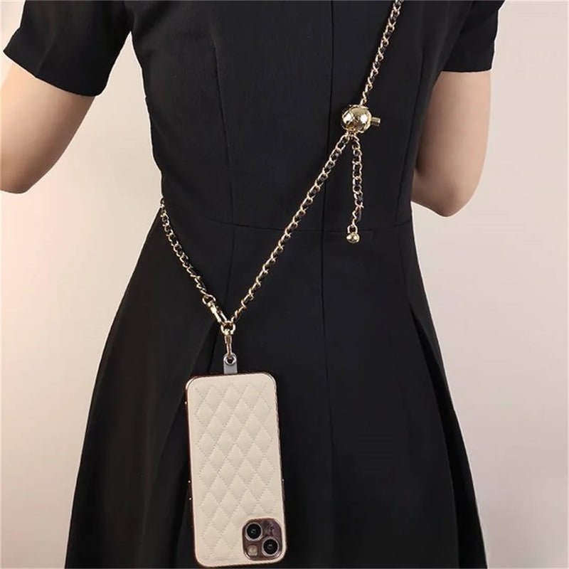 White quilted phone case with crossbodey gold chain on a black dress against a beige background