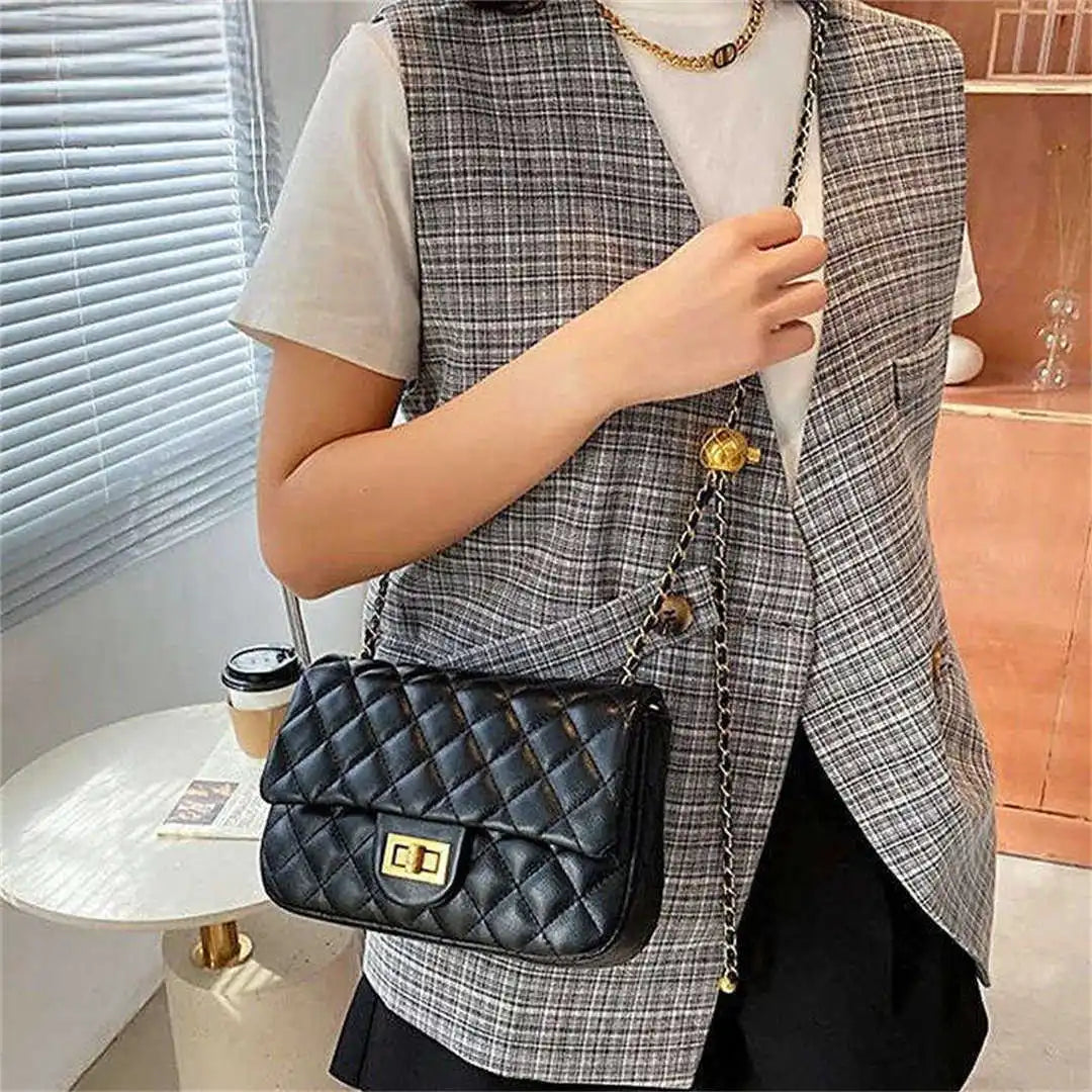 Person wearing a plaid vest holding a black quilted handbag indoors.
