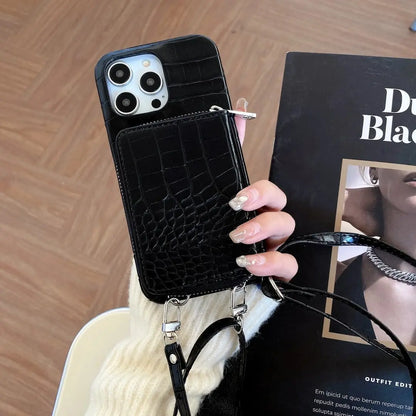 Black crocodile-patterned phone case with a strap held by a hand on a wooden surface.