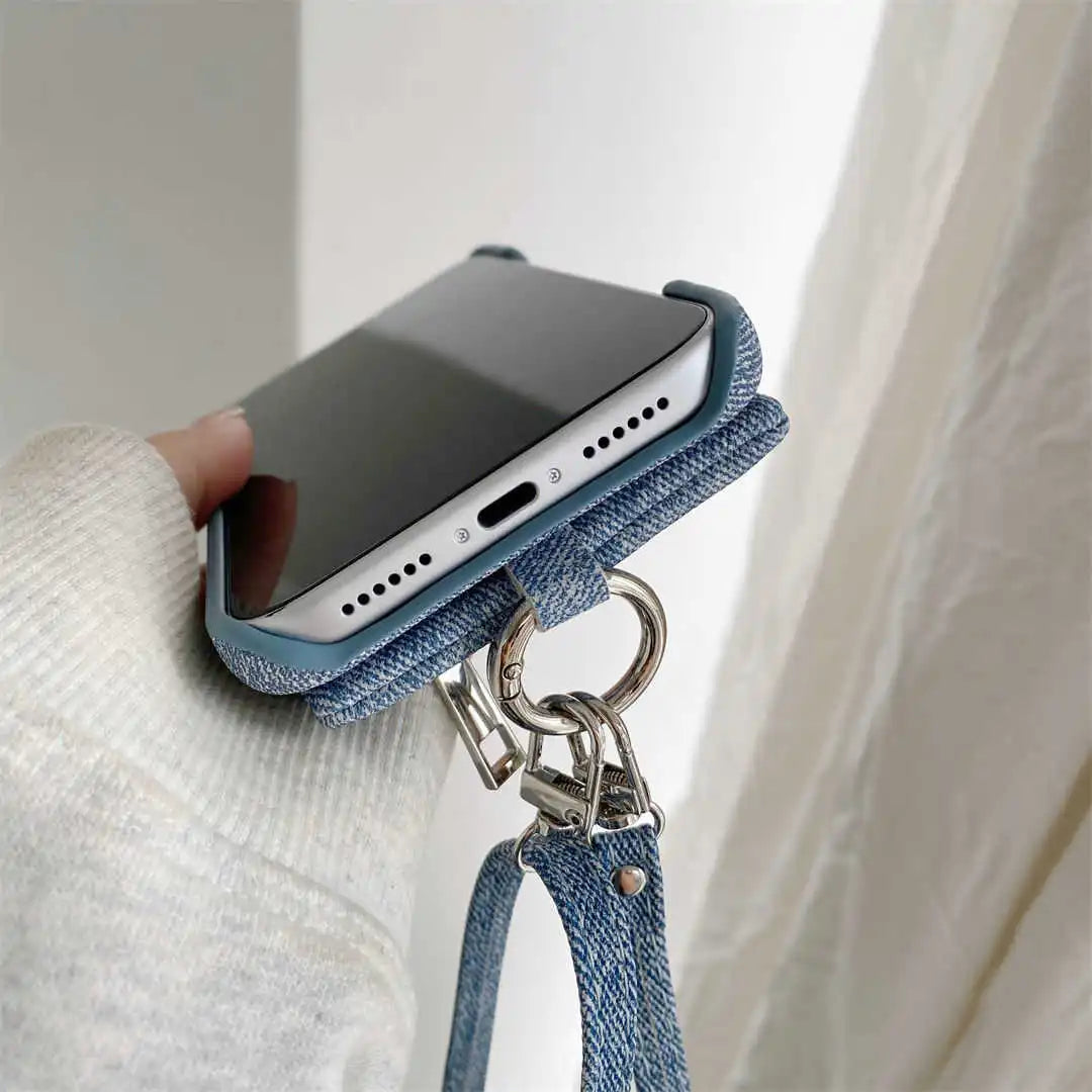 Phone case with denim strap held by a person wearing a white sweater.