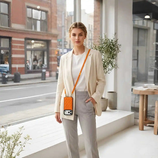 Woman in a beige blazer and gray pants standing on a city street with a bright orange crossbody wallet case.