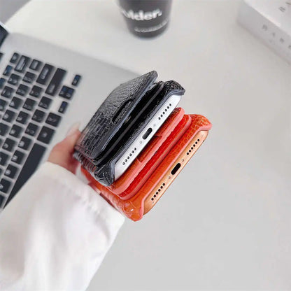 A hand holds a stack of four textured phone cases in black, white, red, and orange, positioned over a light gray desk with a laptop keyboard in the background.