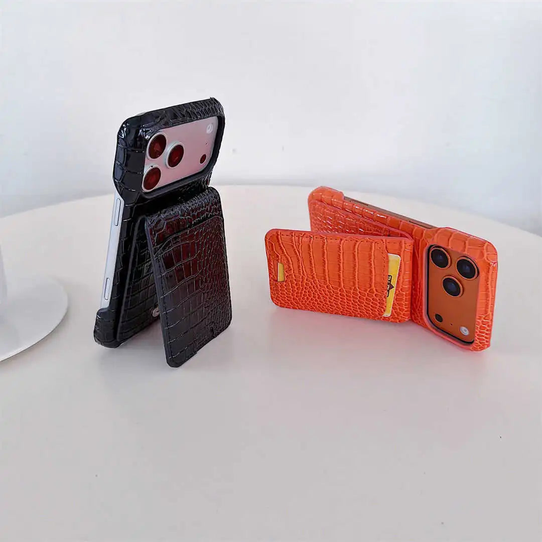 Two phone cases with a crocodile-embossed texture are displayed on a white surface. One case is black and stands open to show a card slot, while the other is orange and shown partially open.
