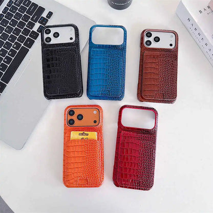 Five phone cases with a crocodile-embossed texture are arranged on a white desk next to a laptop. The cases come in black, blue, brown, orange, and red gradient designs, with two of them featuring card slots.