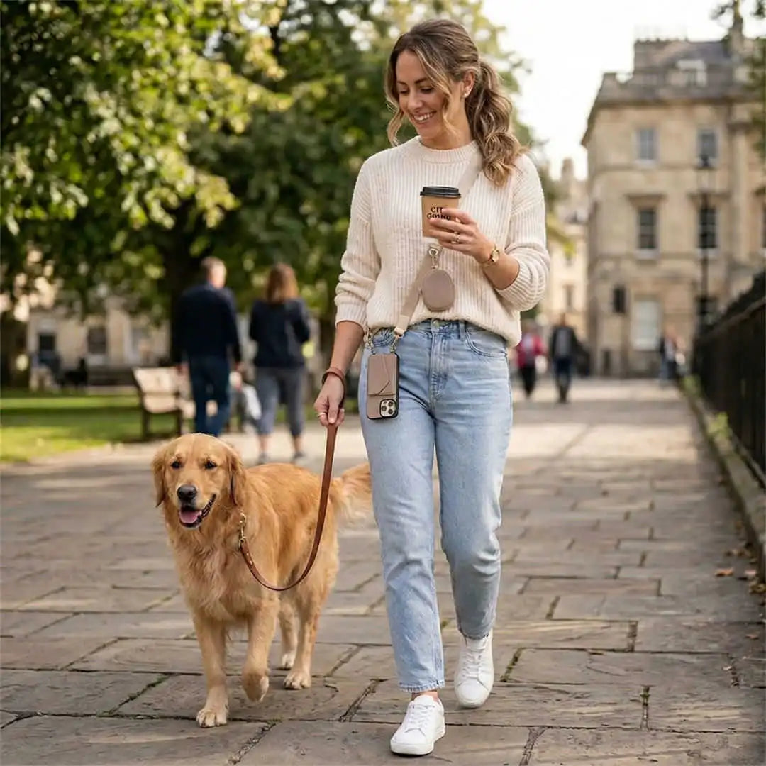 Woman wearing a crossbody wallet system and walking a dog on a city street holding a coffee cup