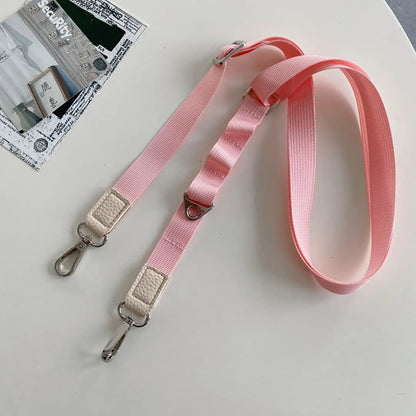 Pink crossbody strap with metal clasps on a light gray surface