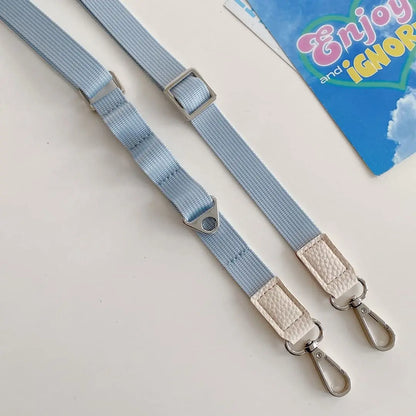 Two light blue straps with metal buckles on a beige surface, with a colorful book titled 'Enjoy and Ignore' in the background.