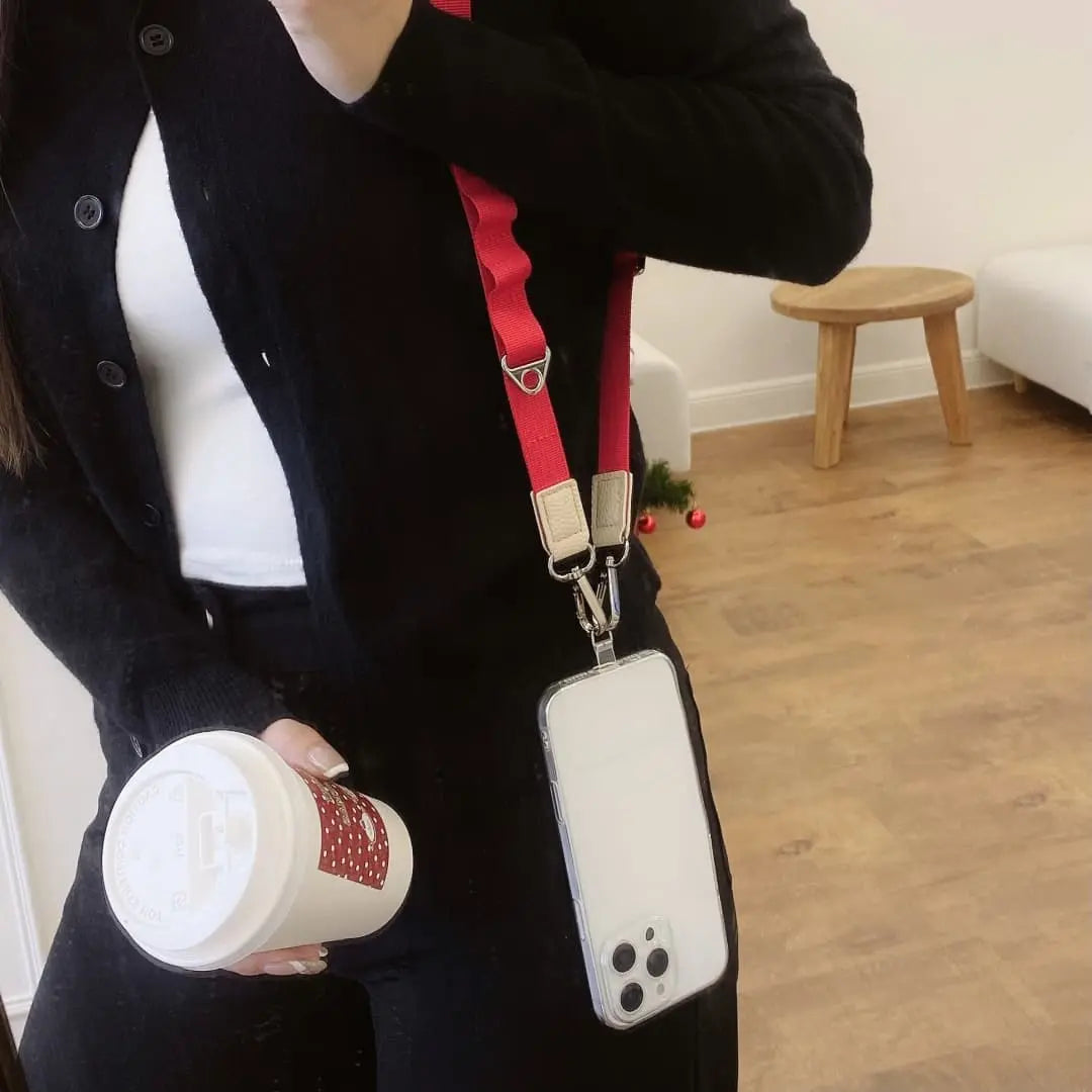 Person holding a coffee cup with a phone case on a strap in a room.